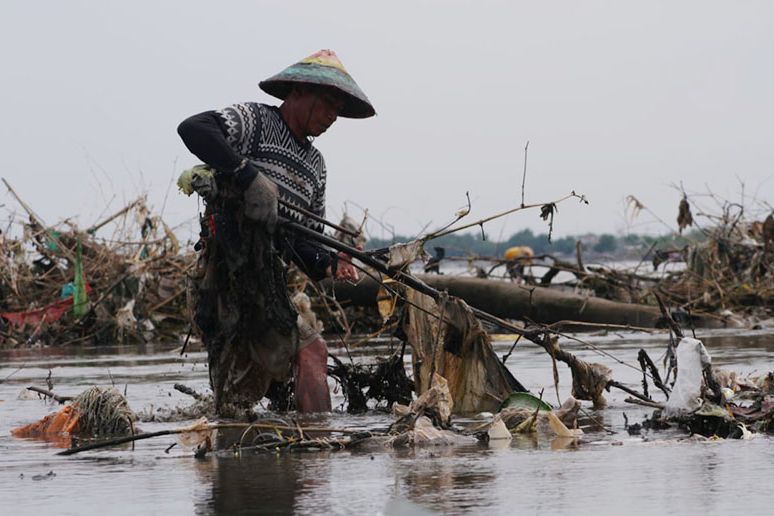 RANTING DAN DAHAN POHON: Muhammad Saha, seorang nelayan besuki membersihkan sampah karena tidak ada jalan untuk perahu melintas. Tumpukan sampai di Pantai Bong pesisir Besuki, Kabupaten Situbondo, Jumat 17 Desember 2021. Foto: Hozaini